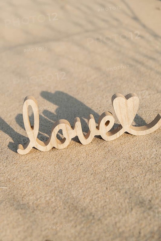 Wooden word love on sandy beach background. Concept of romantic holiday anniversary, proposal, valentines day greeting card, postcard. Letter text in tropical vacation Sand surface. Deep shadows Love is all you need