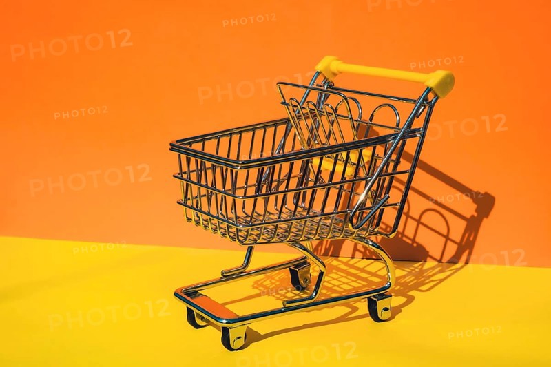 Empty shopping trolley cart on colorful orange yellow background. Copy space for your text. Online shopping, buy mall market shop consumer concept. Small toy supermarket grocery push cart. Food crisis. Rising food cost, grocery prices shortage mass hunger. Inflation