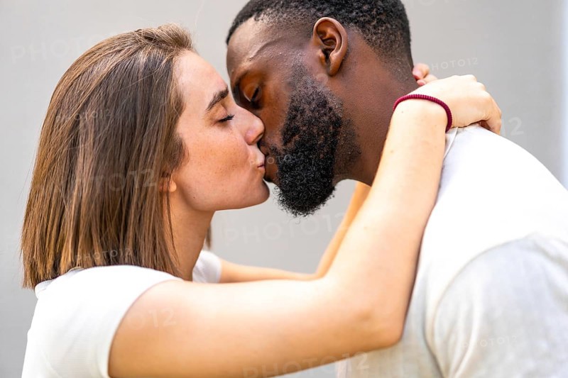 Side view close-up of a multiracial couple of lovers dressed in white kissing tenderly and embracing