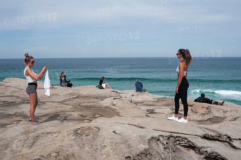 27.09.2019, Sydney, New South Wales, Australia, A young woman takes a photo of her girlfriend on the cliffs at Tamarama Point. Tourists look out to sea in the background. The viewpoint is on the Bondi to Coogee Walk coastal path, Oceania