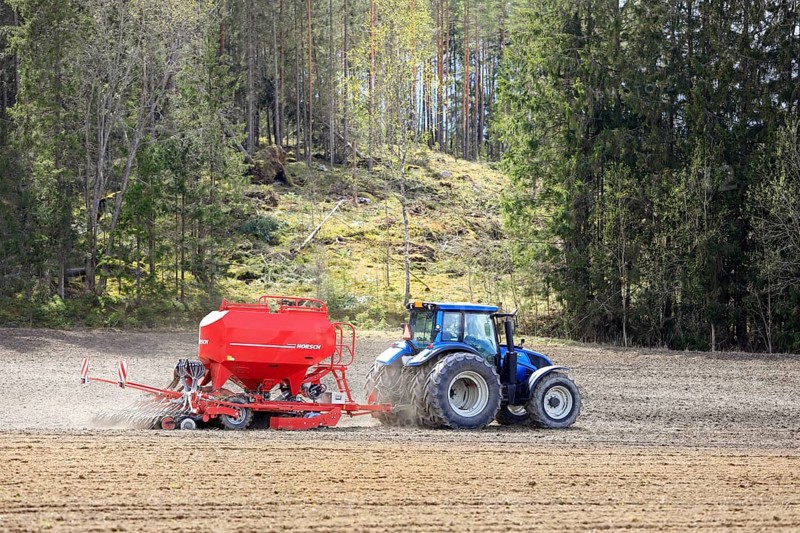 Working in field with blue Valtra tractor and Horsch Pronto 4DC seeder on a day of spring. Salo, Finland. May 14, 2022