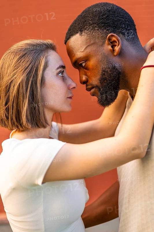 Vertical side view photo of a young African American man and a young Caucasian woman in love are touching faces and looking at each other