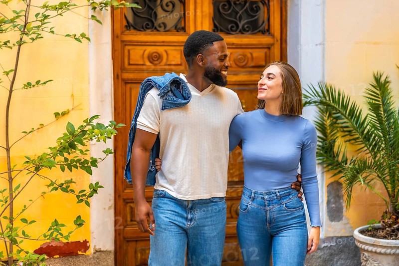 Multi-ethnic couple leaving the house together with a smile, embraced from behind