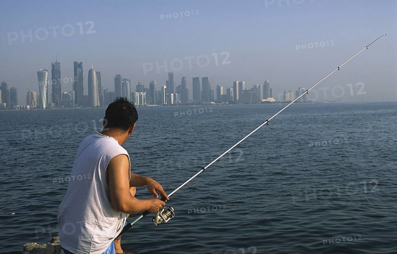 13.09.2010, Doha, Qatar Qatar, A man fishing on the promenade along Al Corniche Street with a view of the skyline of the Al Dafna business district in the background
