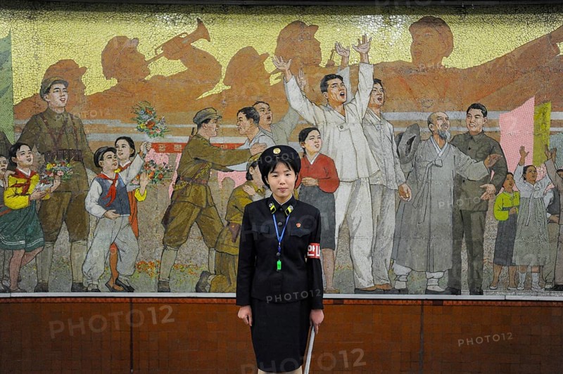 09.08.2012, Pyongyang, North Korea, Asia, A platform supervisor stands in front of a huge mosaic wall at an underground station in Pyongyang. The platform supervisor makes sure that the train runs smoothly and gives the train drivers the signal to continue their journey. They also make sure that nobody stands too close to the tracks, Asia
