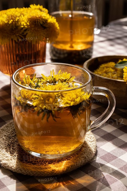 Dandelion flower healthy tea in glass teapot and glass cup on table. Delicious herbal tea from fresh dandelion flowers at home at summer day. Green clearing Hot dandelion tea in a glass teapot. Bouquet of dandelions petals. Wildflowers