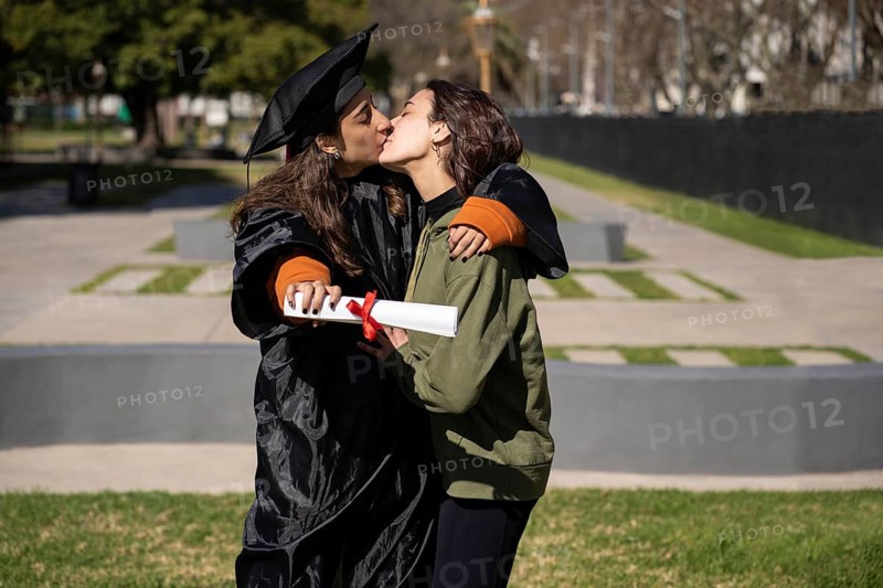Woman recent graduated, dressed in cap and gown, showing off his degree celebrating with her girlfriend