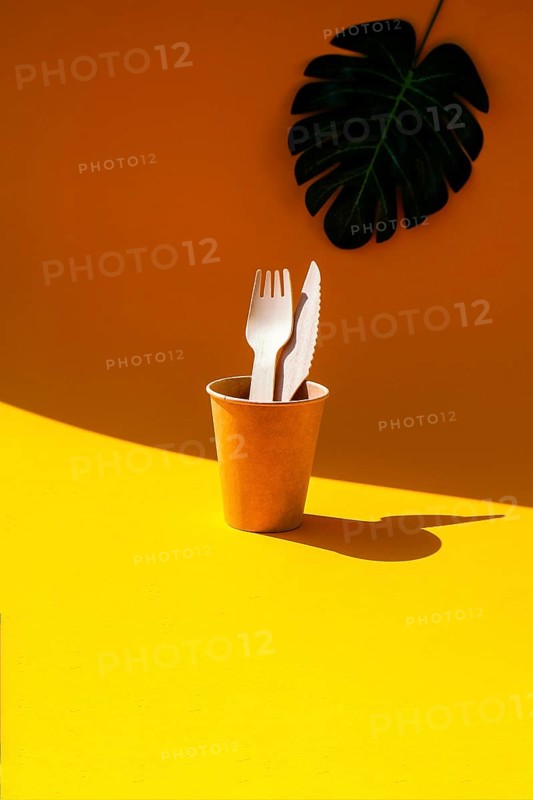 Wooden forks and paper cups with plates on color background. Eco friendly disposable tableware. Used in fast food, restaurants, takeaways, picnics. No plastic Zero waste