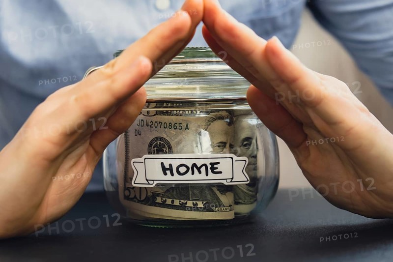 Unrecognizable woman holding Saving Money In Glass Jar filled with Dollars banknotes. HOME transcription in front of jar. Managing personal finances extra income for future insecurity background