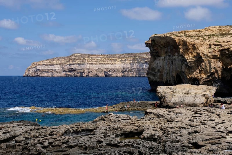 Tourists enjoy the refreshing water under yellowish-brown limestone cliffs, San Lawrenz, Malta, Europe