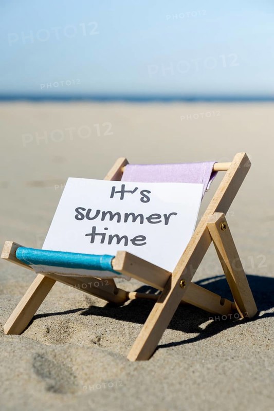 IT'S SUMMERTIME text on paper greeting card on background of beach chair lounge summer vacation decor. Sandy beach sun. Holiday concept postcard. Travel Business concept