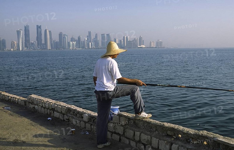 13.09.2010, Doha, Qatar Qatar, A man fishing on the promenade along Al Corniche Street with a view of the skyline of the Al Dafna business district in the background