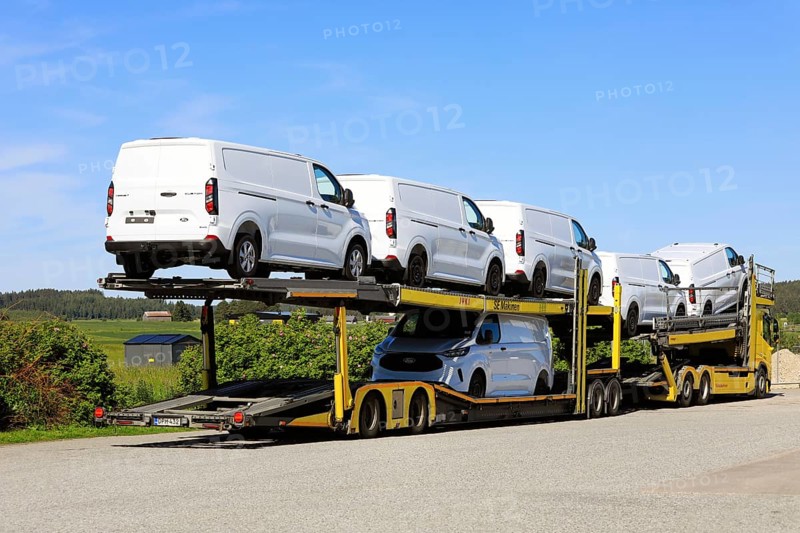 Yellow Volvo vehicle carrier truck transports six new, white Ford Transit Custom vans on trailer, rear view. Salo, Finland. June 22, 2024