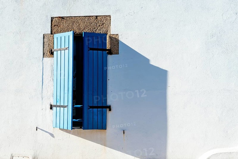 Old window with wooden blue painted shutters on white painted wall