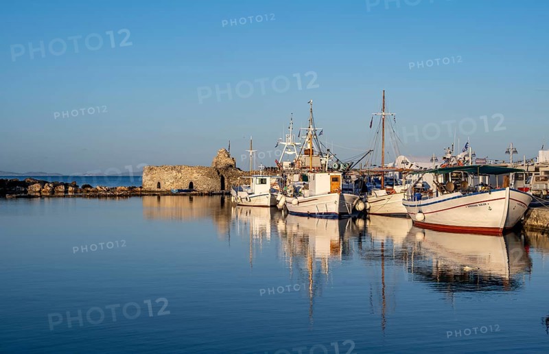 Fishing boats in the harbour and ruins of the Venetian castle, reflected in the sea, at sunset, Naoussa, Paros, Cyclades, Greece, Europe
