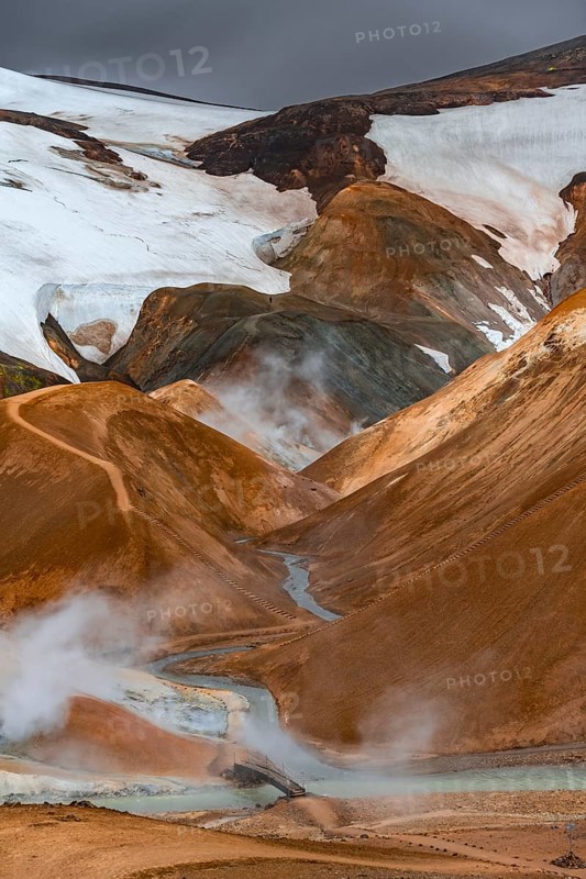 Bridge over steaming stream between colourful rhyolite mountains with snowfields, Hveradalir geothermal area, Kerlingarfjöll, Icelandic highlands, Iceland, Europe