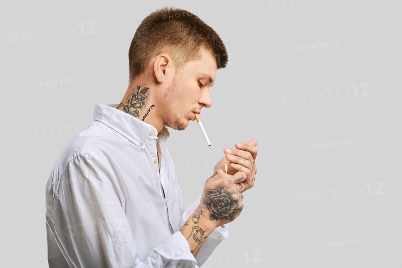 Young tattooed man lights a cigarette in the studio