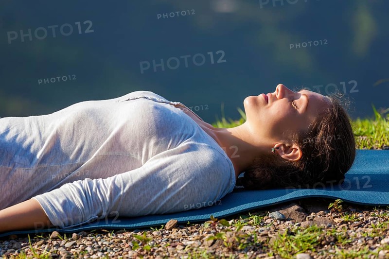 Woman relaxes in yoga relaxation asana Savasana, corpse pose outdoors in Himalayas. Himachal Pradesh, India, Asia