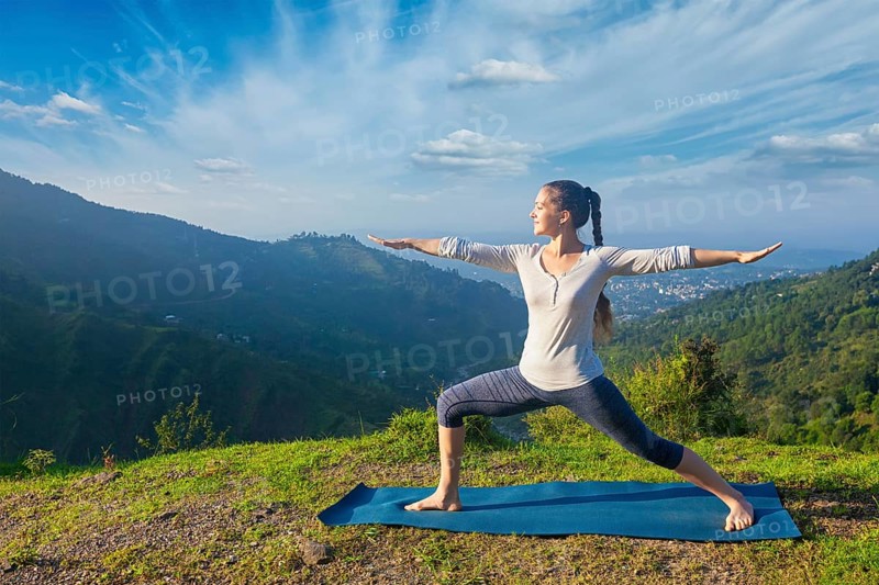 Yoga outdoors, sporty fit woman doing yoga asana Virabhadrasana 2, Warrior pose posture outdoors in Himalayas mountains in the morning