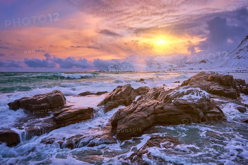 Waves of Norwegian sea on rocky coast in fjord on sunset with sun. Skagsanden beach, Lofoten islands, Norway, Europe