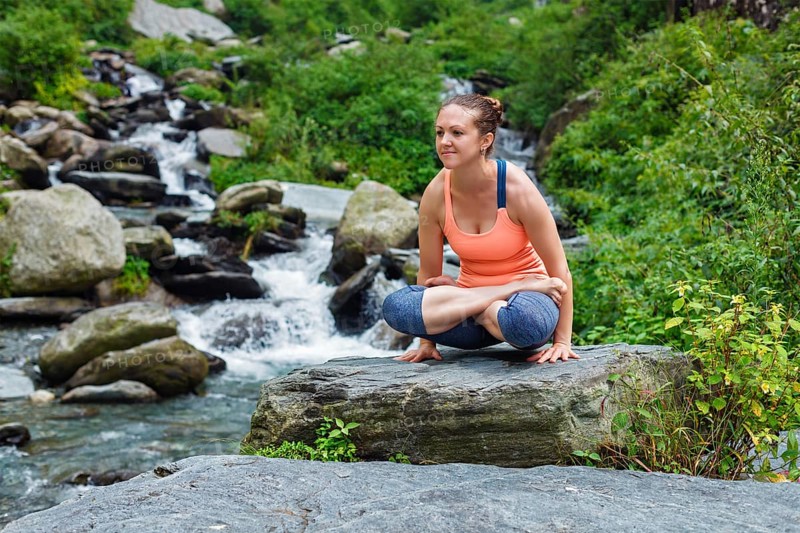 Yoga exercise outdoors, woman doing Ashtanga Vinyasa Yoga arm balance strength training asana Tolasana, scales pose at waterfall in Himalayas