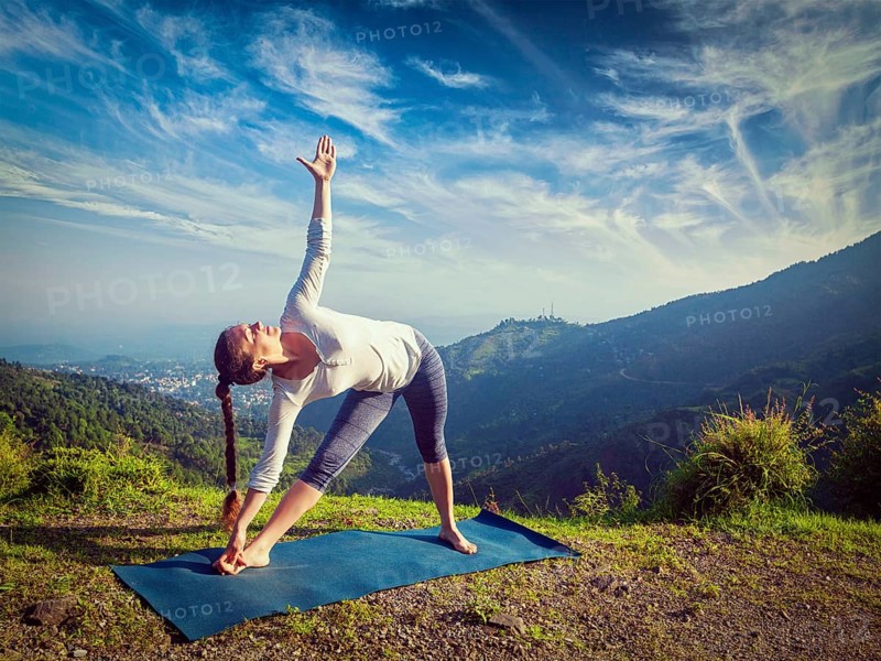Woman doing Ashtanga Vinyasa yoga asana Utthita trikonasana, extended triangle pose outdoors in mountains in the morning. Vintage retro effect filtered hipster style image