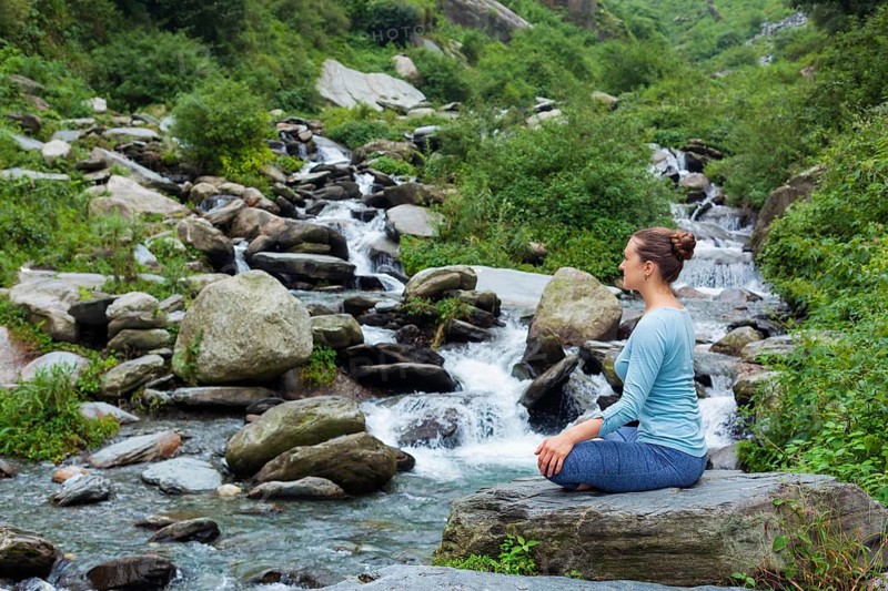 Woman in Hatha yoga asana Padmasana outdoors at tropical waterfall
