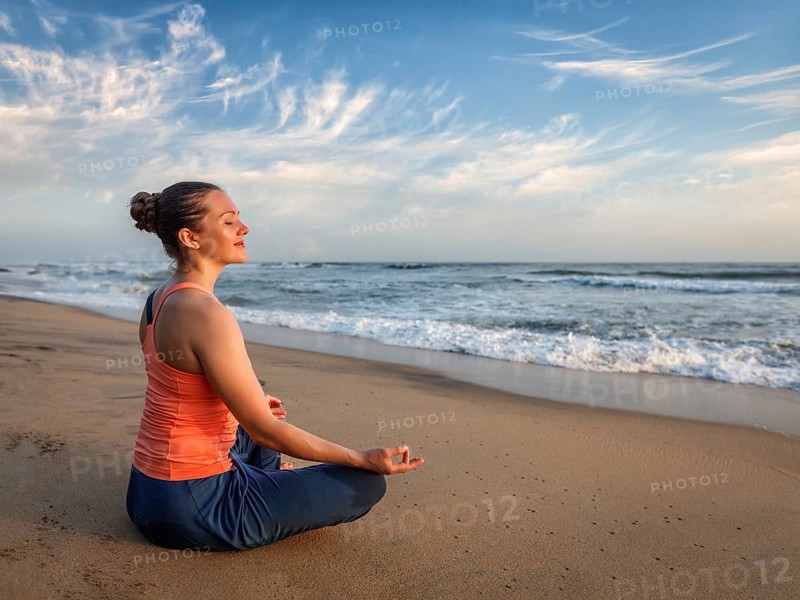 Young sporty fit woman doing yoga, meditating and relaxing in Padmasana Lotus Pose) with chin mudra outdoors at tropical beach on sunset