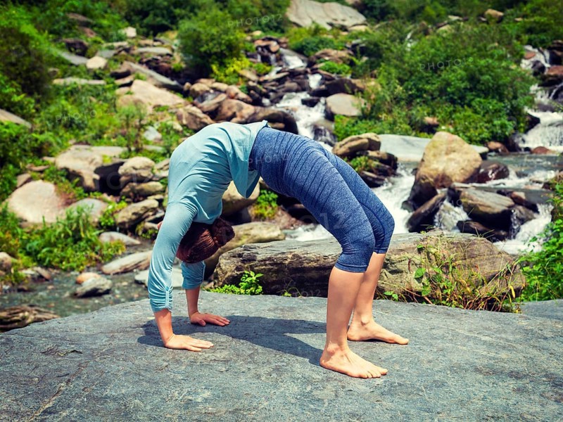 Yoga outdoors, young sporty fit woman doing Ashtanga Vinyasa Yoga asana Urdhva Dhanurasana, upward bow pose at tropical waterfall. Vintage retro effect filtered hipster style image