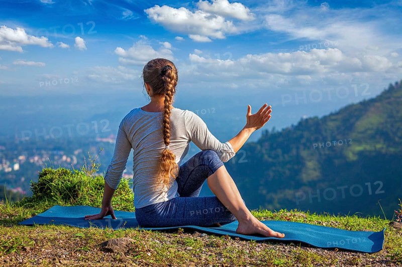 Hatha yoga outdoors, woman doing yoga asana Parivrtta Marichyasana or ardha matsyendrasana, seated spinal twist outdoors in mountains in the morning