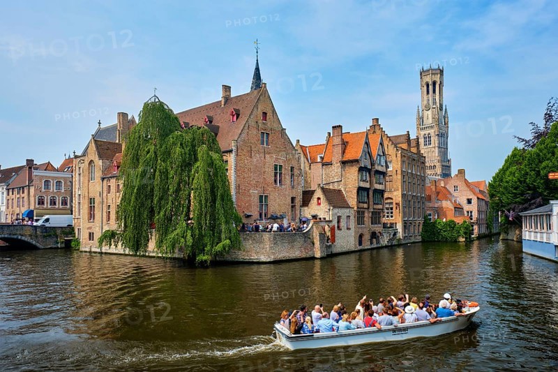 Bruges, Belgium, May 29, 2018: Tourist boat passin in famous Bruges tourist landmark, Rozenhoedkaai canal with Belfry and old houses along canal, Europe