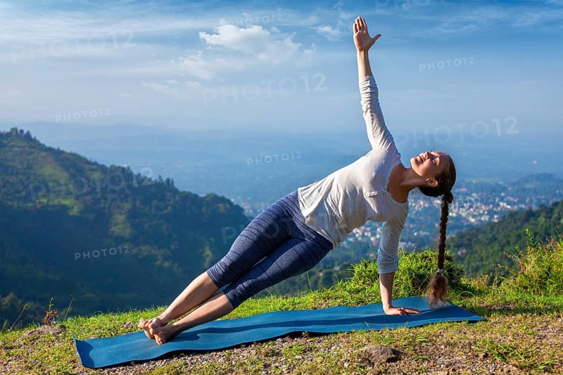 Yoga outdoors, beautiful sporty fit woman doing yoga asana Vasisthasana, side plank pose in mountains