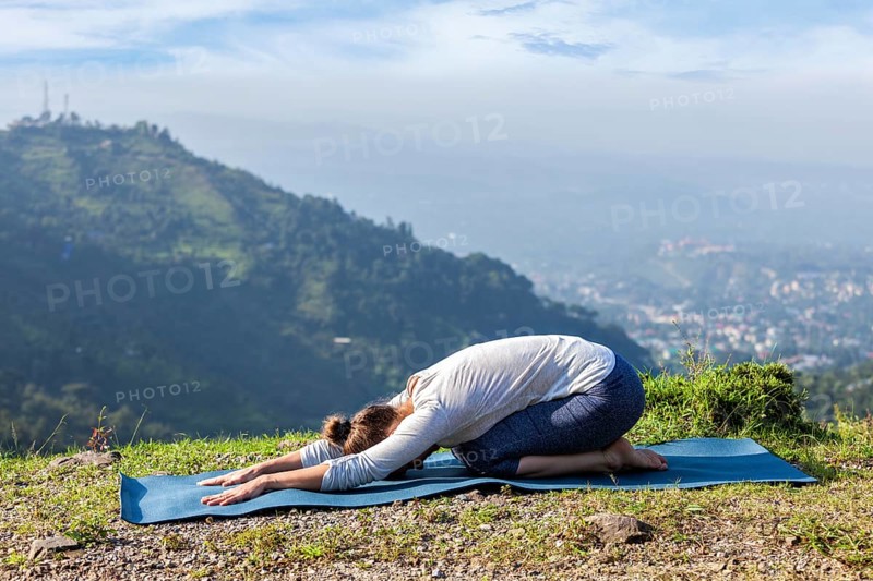 Sporty fit woman practices yoga asana Balasana, child pose outdoors in mountains