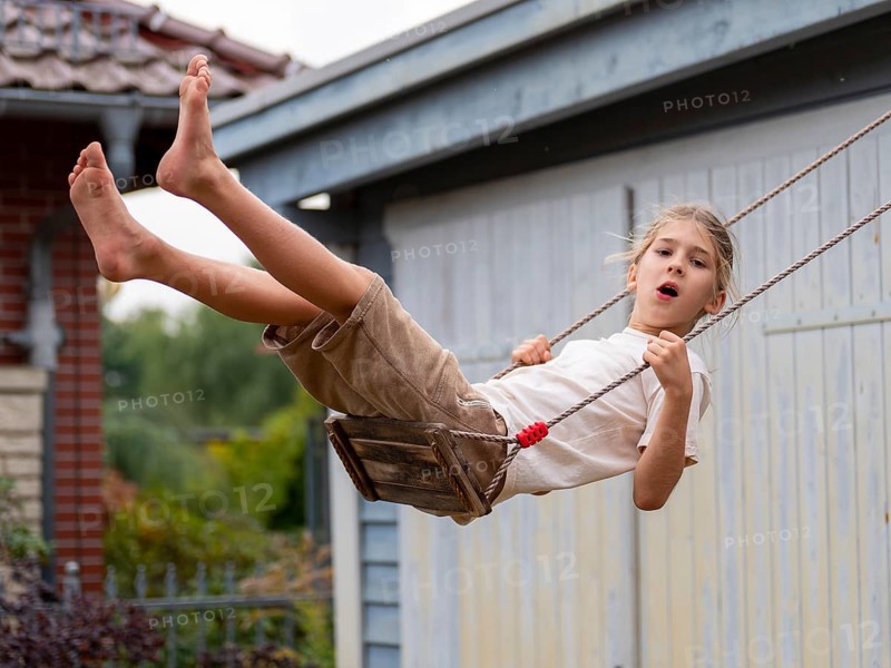 Boy swinging while sitting on children's swing at shed and garden gate, Germany, Europe