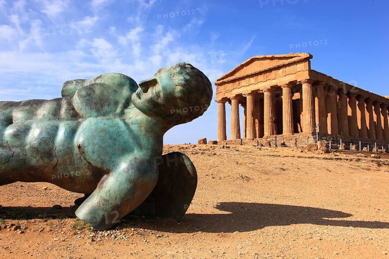 In the Parco Valle dei Templi di Agrigento, Unesco World Heritage Site, remains of the ancient city of Akragas in the Valley of the Temples of Agrigento, the Temple of Concordia with the sculpture of the crashed Icarus by artist Igor Mitorgi, installed in 2012, Sicily, Italy, Europe
