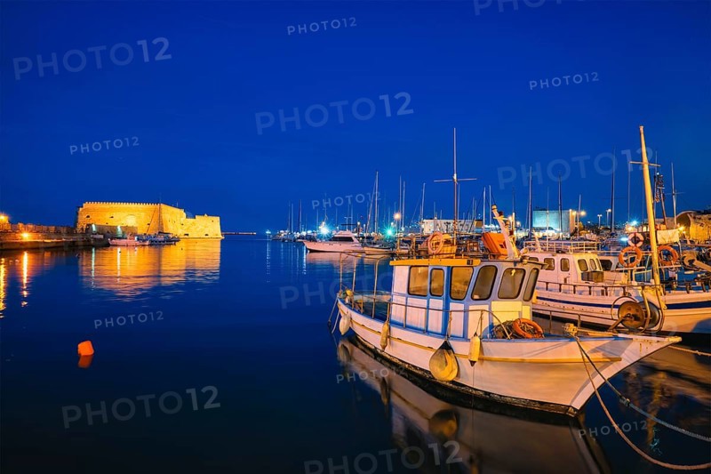 Venetian Fort castle in Heraklion and moored Greek fishing boats in port, Crete Island, Greece in the evening