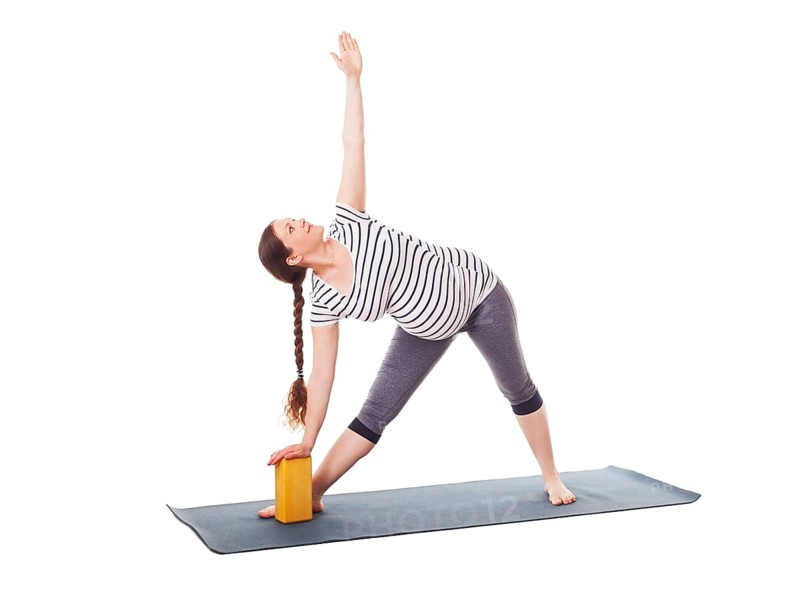Pregnancy yoga exercise, pregnant woman doing asana Utthita trikonasana, extended triangle pose with block isolated on white background