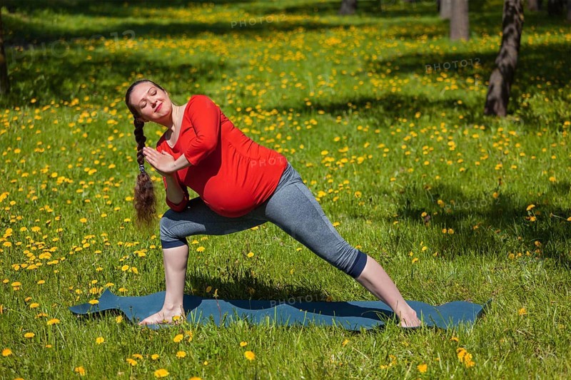 Pregnancy yoga exercise, pregnant woman doing asana Utthita parsvakonasana outdoors on grass in summer