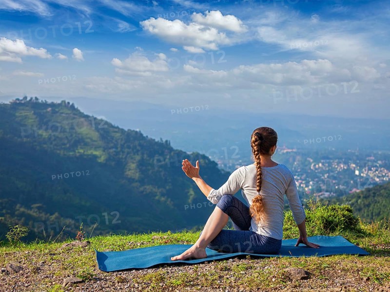 Hatha yoga outdoors, sporty fit woman doing yoga asana Parivrtta Marichyasana (or ardha matsyendrasana), seated spinal twist outdoors in mountains in the morning