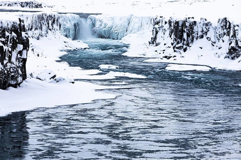 Selfoss waterfall with the river Jökullsa a Fjöllum, icy and snow-covered cliffs and shoreline, Northern Iceland Eyestra, Iceland, Europe