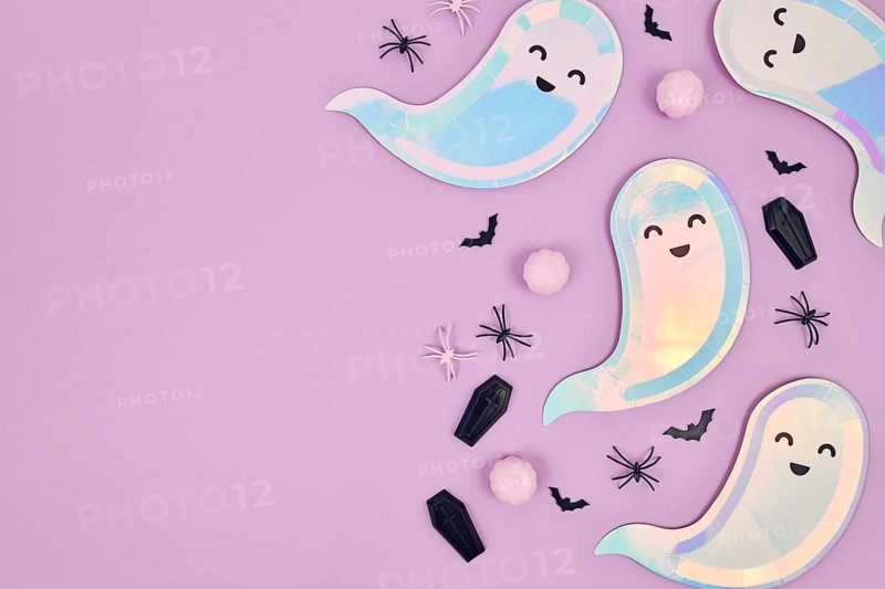 Cute pastel colored Halloween party flat lay with ghost shaped plates, spiders, pumpkins and coffins on violet background