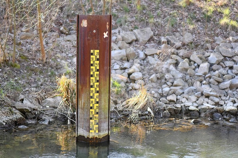 Yellow metric flood level marker in river with low water level
