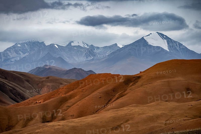 View over red mountainous landscape, high mountains with snow, dramatic dark clouds, Konorchek Canyon, Chuy, Kyrgyzstan, Asia