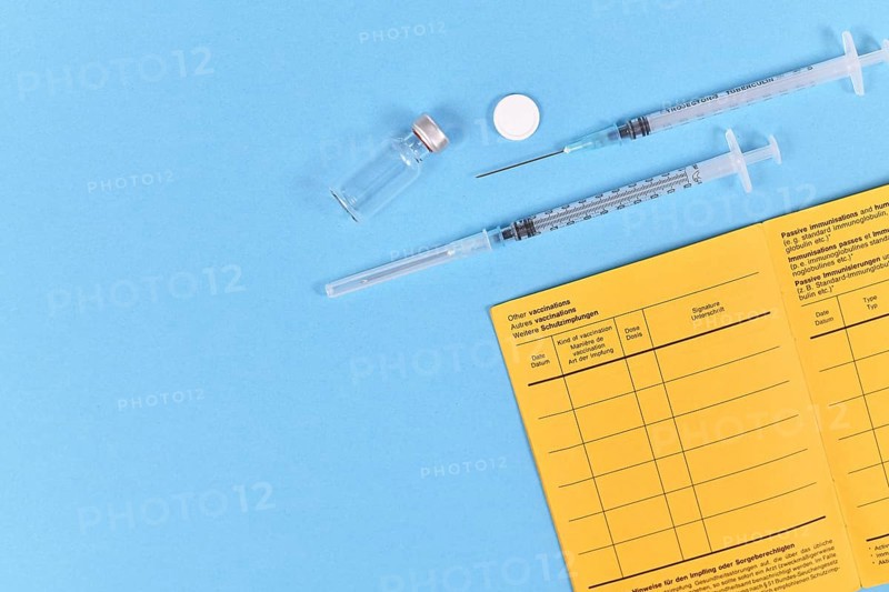 Vaccine concept with syringe, vial and yellow international certificate of vaccination on blue background with copy space