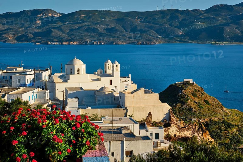Picturesque scenic view of Greek town Plaka on Milos island over red geranium flowers and Orthodox greek church. Plaka village, Milos island, Greece, Europe