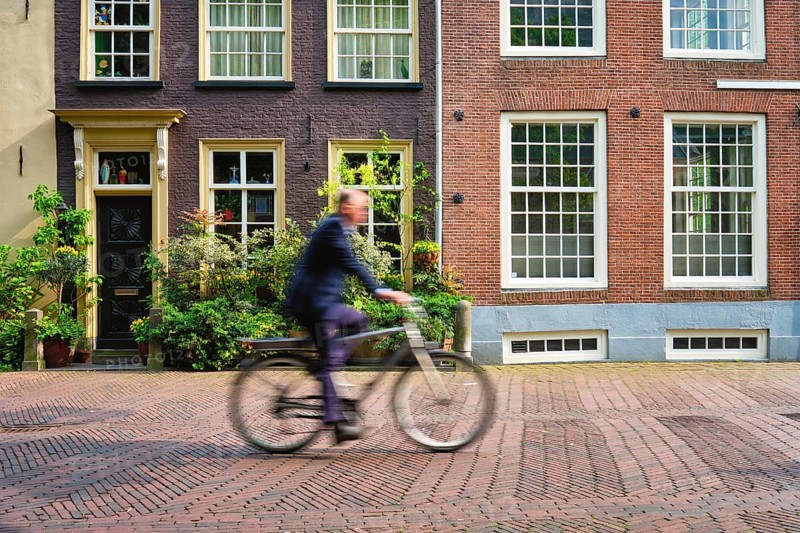 Motion blurred bicycle rider cyclist man on bicycle very popular means of transport in Netherlands in street with old houses of Delft, Netherlands