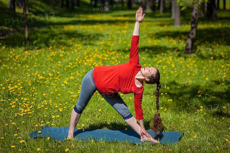 Pregnancy yoga exercise, pregnant woman doing asana Utthita trikonasana outdoors on grass in summer