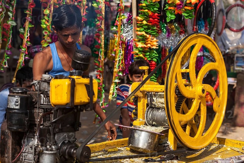 PUSHKAR, INDIA, NOVEMBER 20, 2012: Street vendor makes sugarcane juice by crushing peeled sugar cane in a mill in Pushkar, Rajasthan, India, Asia