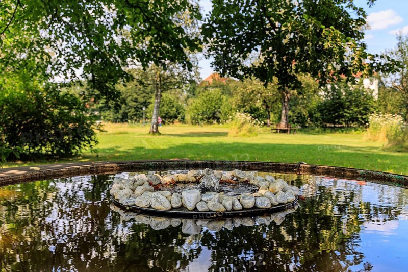 Small fountain and water bowl with stones under trees, Schlehdorf Monastery, Bavaria, Germany, Europe