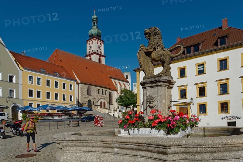 Fountain with lion statue on a sunny market square with church in the background and walking woman, Luitpoldplatz, St. Marien parish church, Sulzbach Rosenberg, Bavaria, Germany, Europe